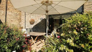Un patio al aire libre con una mesa y un paraguas, rodeado de abundante vegetación y un muro de piedra.
