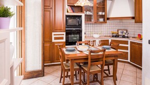 A kitchen with wooden cabinets, a dining table with chairs, a microwave, and a stove. - Relax overlooking Lake Garda (Bardolino)