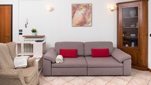 A living room with a beige sofa, red cushions, a wooden cabinet, and a wall-mounted air conditioner. - Relax overlooking Lake Garda (Bardolino)