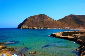 A coastal landscape with clear turquoise waters, rocky terrain, and a mountain in the background.