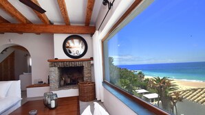 A cozy room with a stone fireplace, a large window overlooking a beach, and a view of the ocean. - Exclusive villa on the beach front. FREE WIFI (Tarifa)