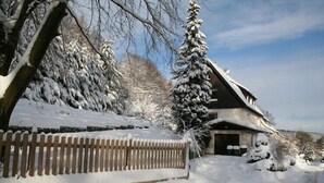 Ett snötäckt bostadsområde med ett hus, ett trästaket och snötyngda träd.