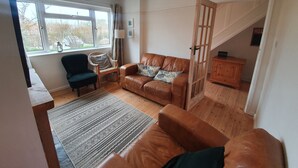 A living room with a brown leather sofa, a dark armchair, a patterned rug, and a wooden cabinet.