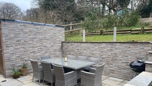 A patio with a stone table and wicker chairs, a barbecue grill, and a stone wall.