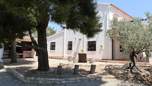 Un edificio bianco con tetto in tegole, circondato da alberi e un cortile in ghiaia.