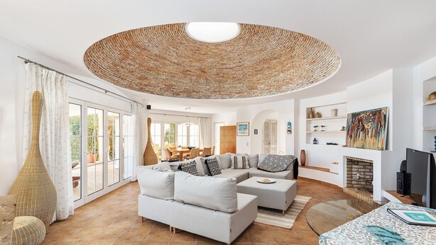 A spacious living room with a large sofa, a coffee table, and a TV. There is a fireplace and a large window with curtains. - Villa Dome OCV - Private Heated Pool (Albufeira)