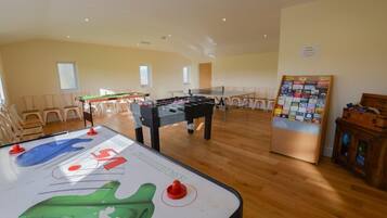 A room with a foosball table, a pool table, and a bulletin board with various notices.