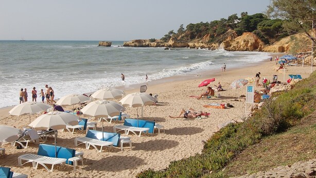 Una playa con tumbonas y sombrillas, acantilados rocosos y el mar.