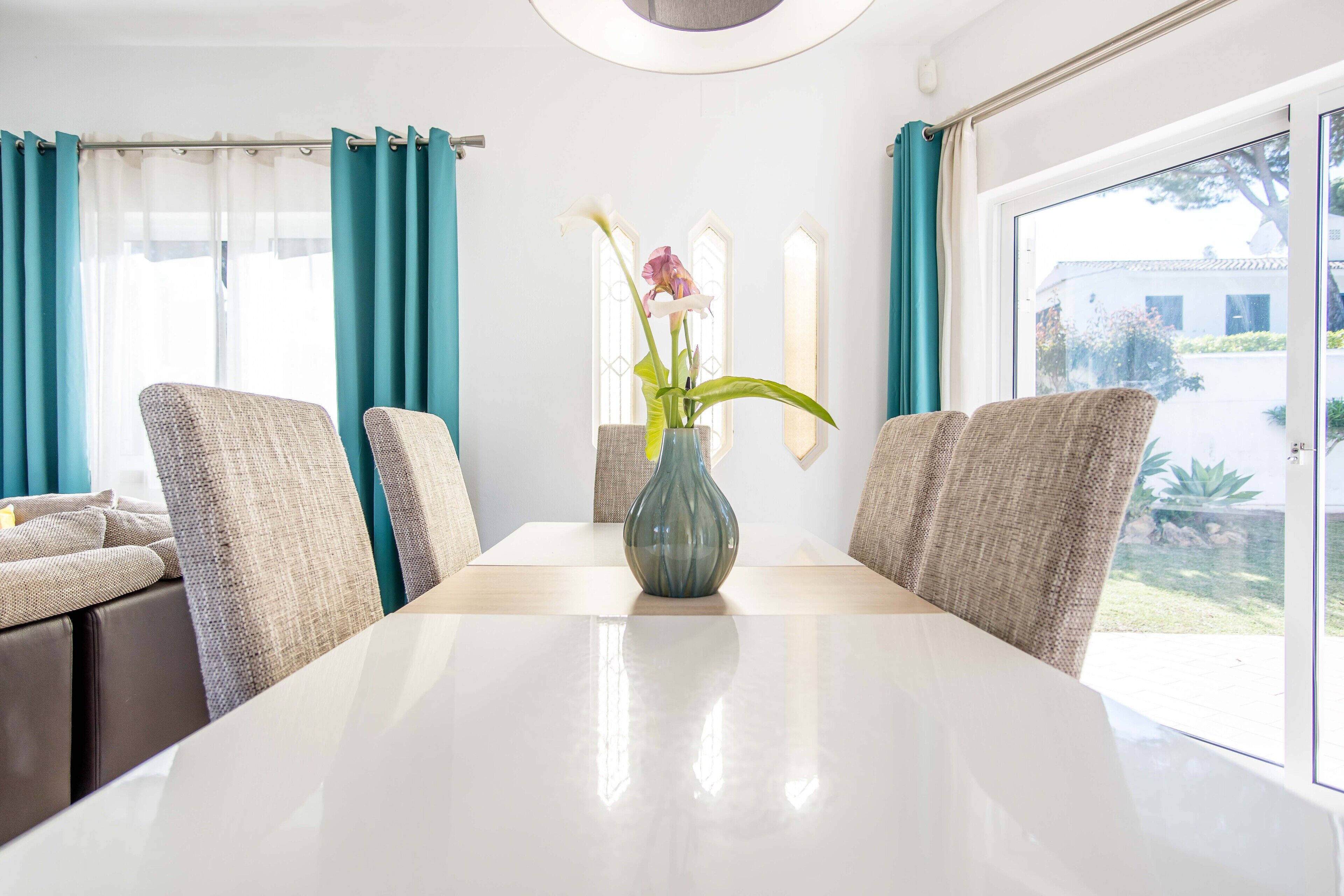 A dining area with a white table, teal curtains, and wicker chairs.