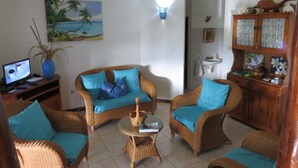 Ein Wohnzimmer mit Rattanmöbeln, einem Gemälde, einem Fernseher und einer Kommode mit Dekorationsobjekten.