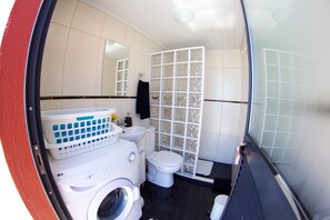 A compact bathroom with a washing machine, a toilet, and a shower enclosure. - Bungalow with heated saltwater pool (Calheta)