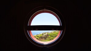 Une fenêtre ronde donnant sur un paysage verdoyant et des bâtiments.