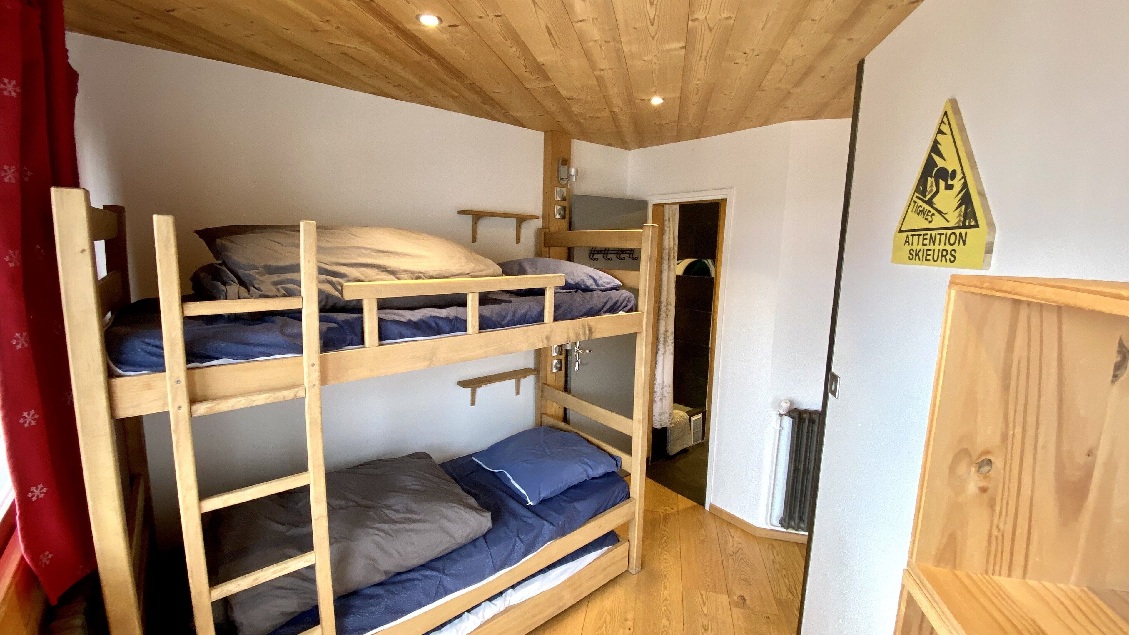 Habitación con literas de madera, un radiador y un cartel de precaución en la pared.