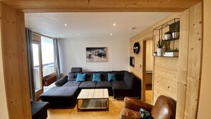 Een moderne woonkamer met een hoekbank, een salontafel, een leren fauteuil en een houten wand.