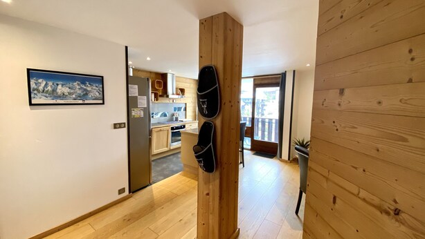 Een gang met houten vloeren, een keukenhoek met houten kastjes, en een deur naar een balkon.