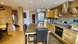 Een moderne keuken met houten kastjes, een roestvrijstalen koelkast, een oven en een eethoek met een tafel en stoelen.
