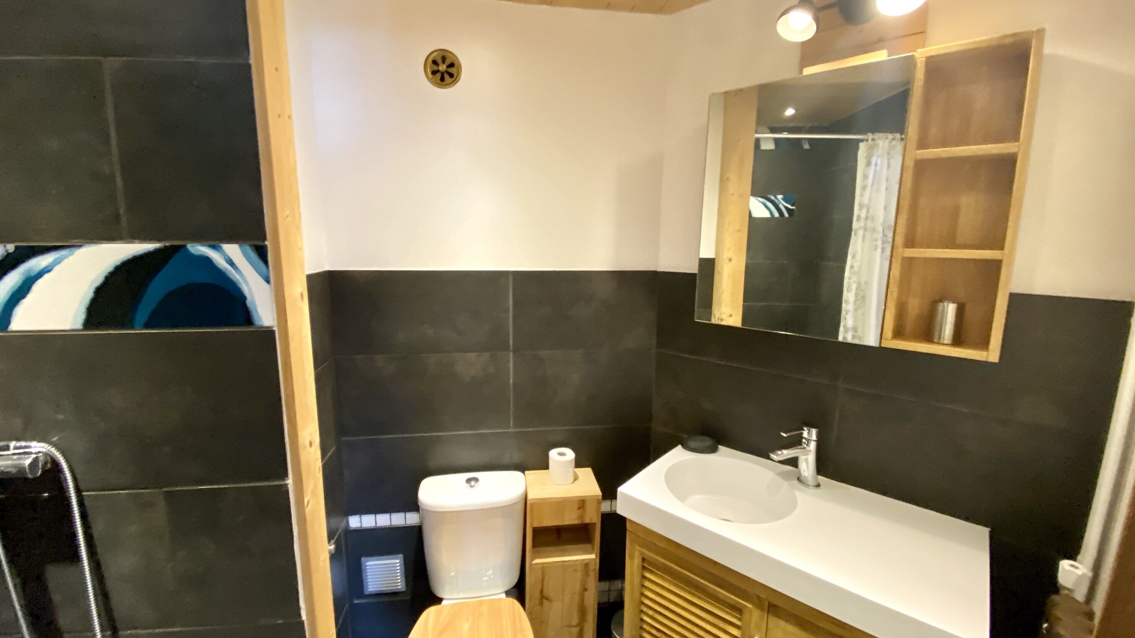 Un bagno moderno con lavandino bianco, piastrelle scure e un mobile contenitore in legno.