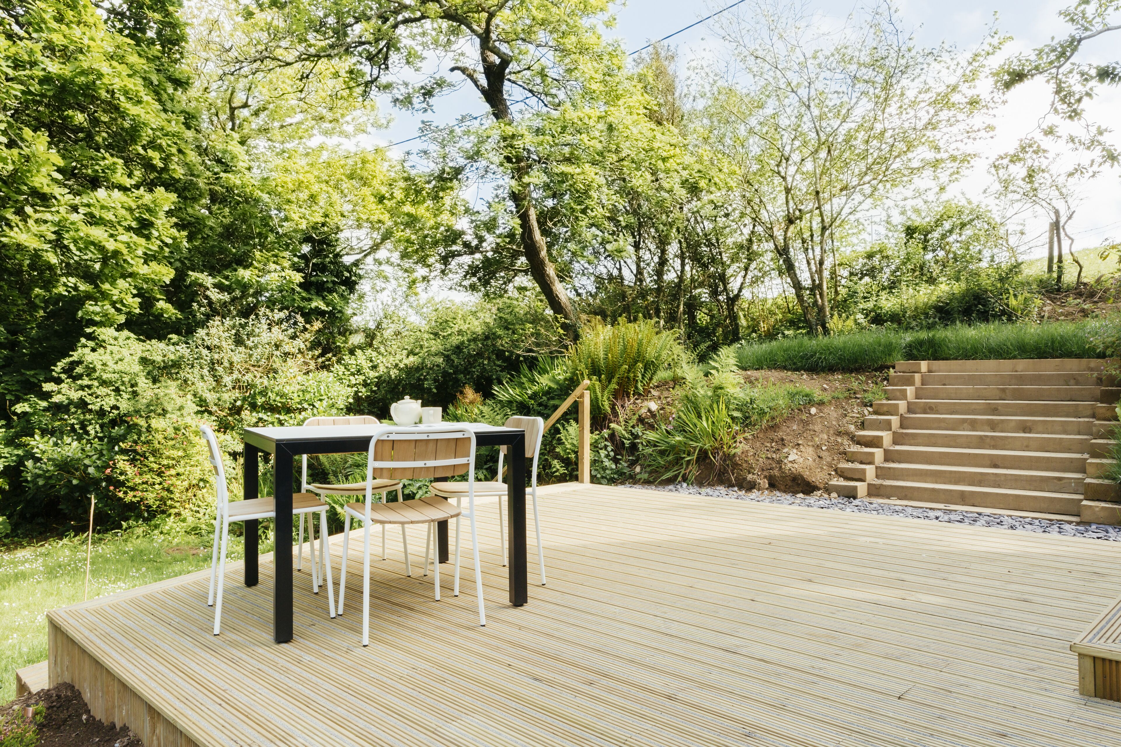 Eine Holzterrasse mit Tisch und Stühlen, umgeben von üppiger Bepflanzung und einer Treppe.
