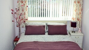 A bedroom with a bed, two pillows, a nightstand, a lamp, and a vase with flowers. - Mayfield  stay 4 to 30     days maybe  longer .car parking for 2 cars  on  drive (Thornton Cleveleys)