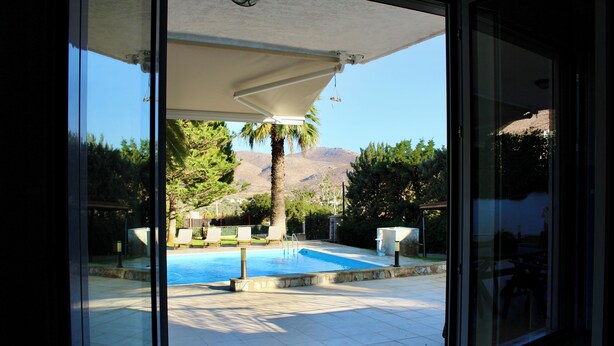 Une vue sur une piscine avec un patio couvert, entourée de verdure et avec des montagnes en arrière-plan.
