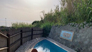 Une piscine bordée de pierres, une clôture en bois et un mur de pierres agrémenté de motifs en carreaux.
