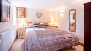 A bedroom with a large bed, two bedside tables with lamps, a wooden cabinet, a heart-shaped wall decoration, and a mirror. - Bay Cottage, a section of Ebbingford Manor, 850 yr old manor house by beach&town (Bude)