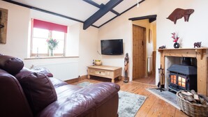 A cozy living room with a leather sofa, a television, a fireplace, and a wooden ceiling. - Bay Cottage, a section of Ebbingford Manor, 850 yr old manor house by beach&town (Bude)