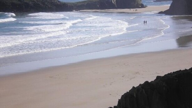 Een strand met rotsformaties en golven.