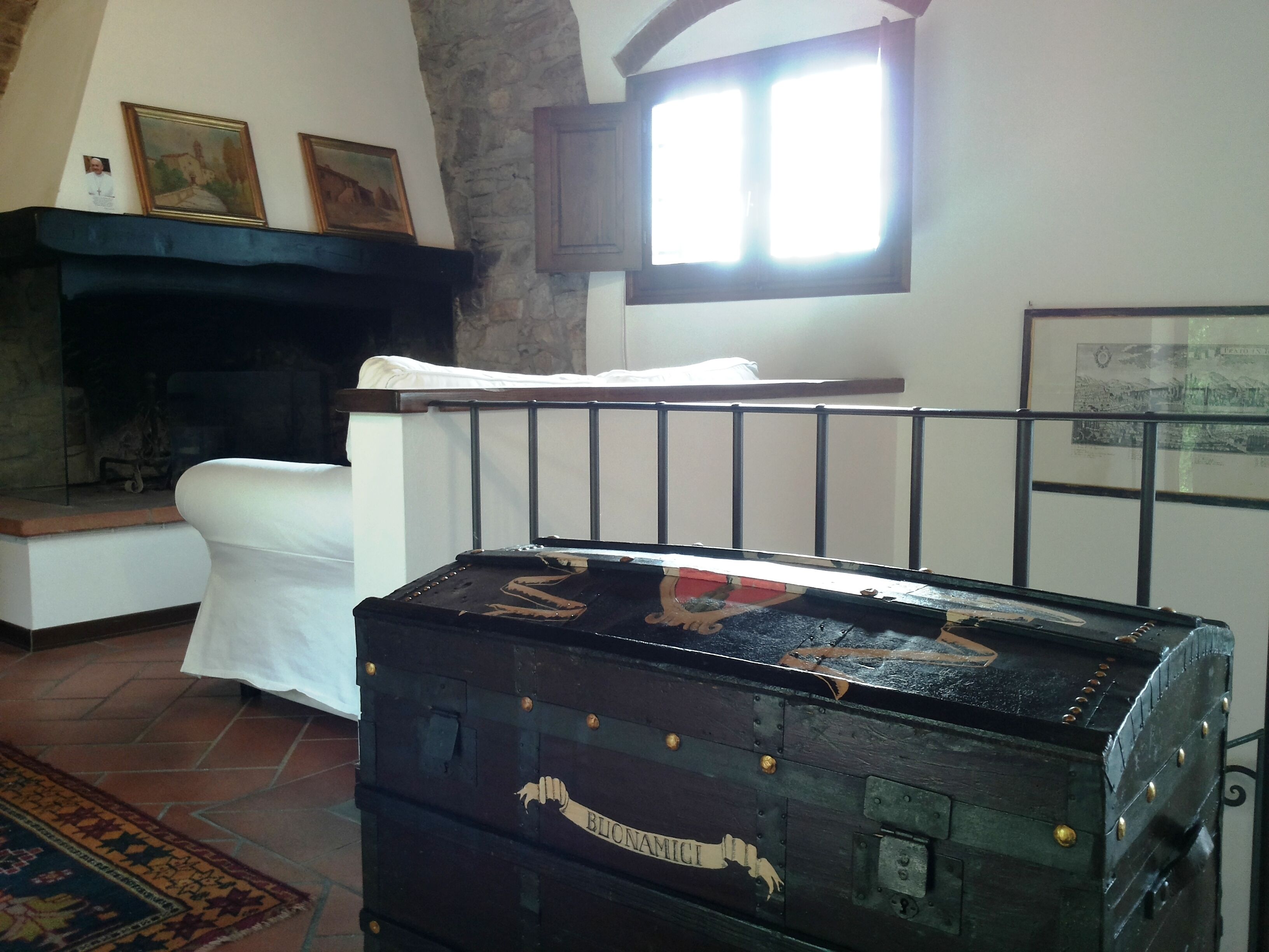 A room with a fireplace, a large black trunk, and a window with curtains.
