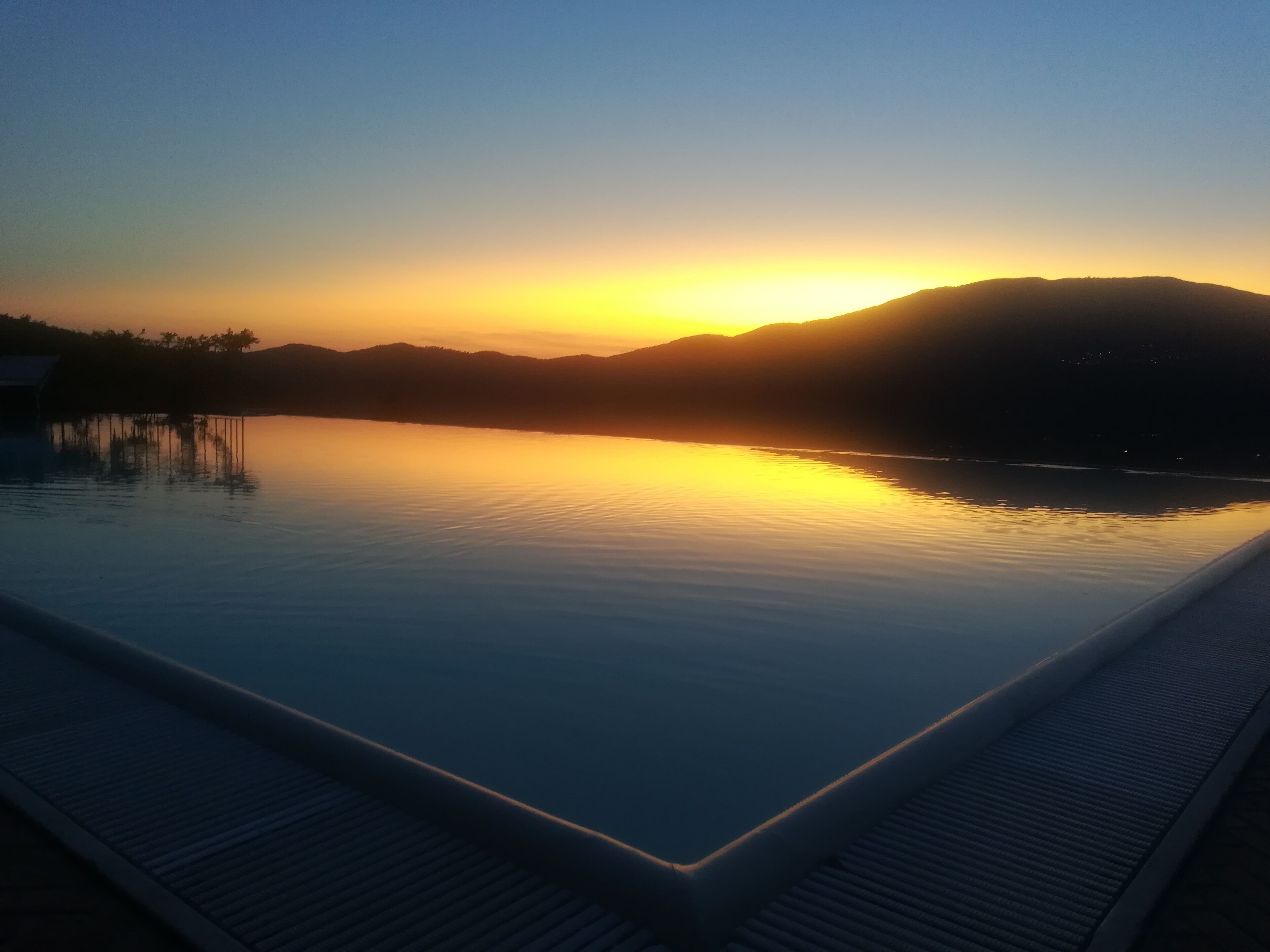 A serene infinity pool with a clear view of the sunset over the water.