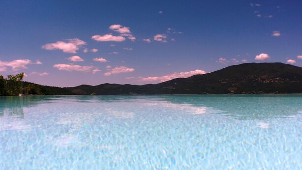 Vista despejada de una piscina con agua tranquila, rodeada de montañas y un cielo claro.
