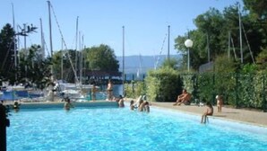 Ein Schwimmbecken mit Personen, umgeben von Grünpflanzen und blauem Himmel.