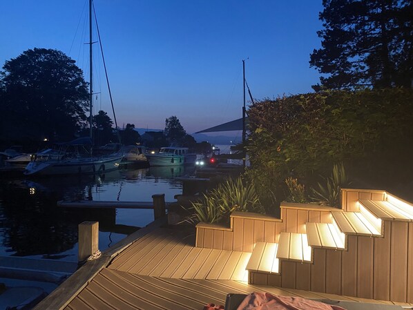 A wooden dock with steps leading into the water, surrounded by greenery and boats.