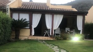 A house with a covered porch, a lawn, and a stone pathway leading to the entrance. - Villa with garden just 200 meters from the beautiful beach of Costa Rei (Costa Rei)