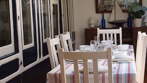A dining area with a table set for four, white chairs, and a vintage Coca-Cola sign on the wall. - Beach front location, Pet friendly, Full of charachter, Private garden, Sea view (Selsey)