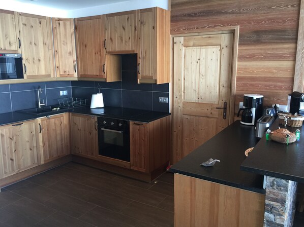 A kitchen with wooden cabinets, a black countertop, a stove, a sink, and a coffee maker.
