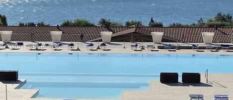 A large swimming pool with sun loungers and a view of the sea.