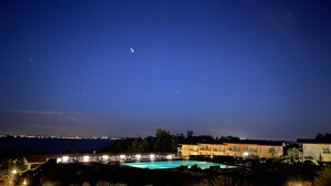 Vue nocturne d’un hôtel avec une piscine, un éclairage extérieur et, en arrière-plan, le panorama de la ville.