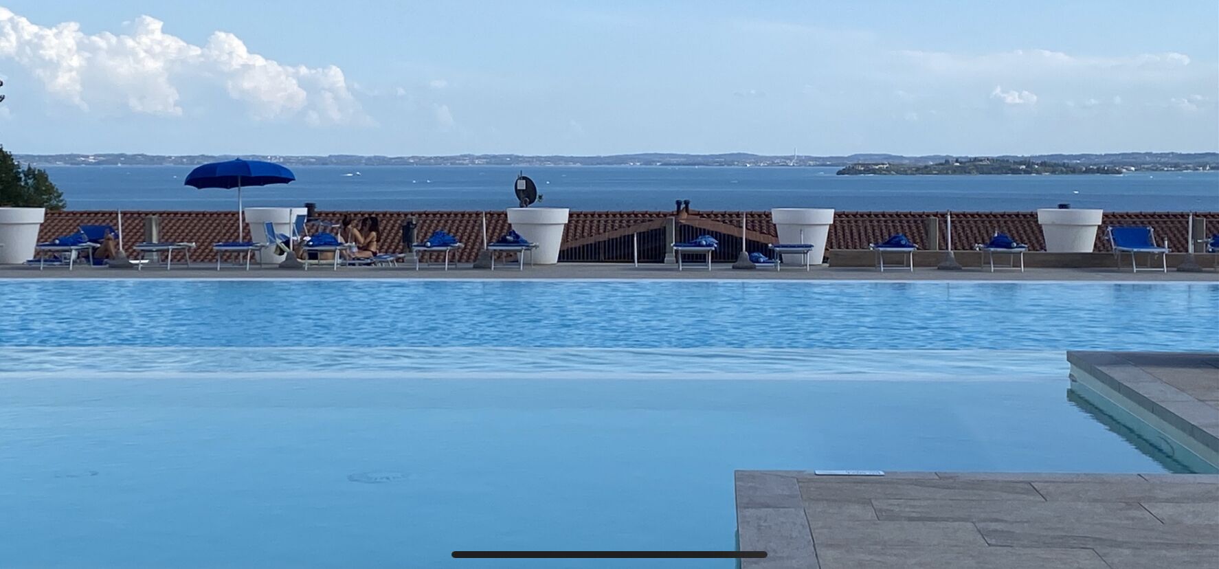 Zona junto a la piscina con sillas de descanso y sombrillas, vista al mar y una estructura de techo con tejas.