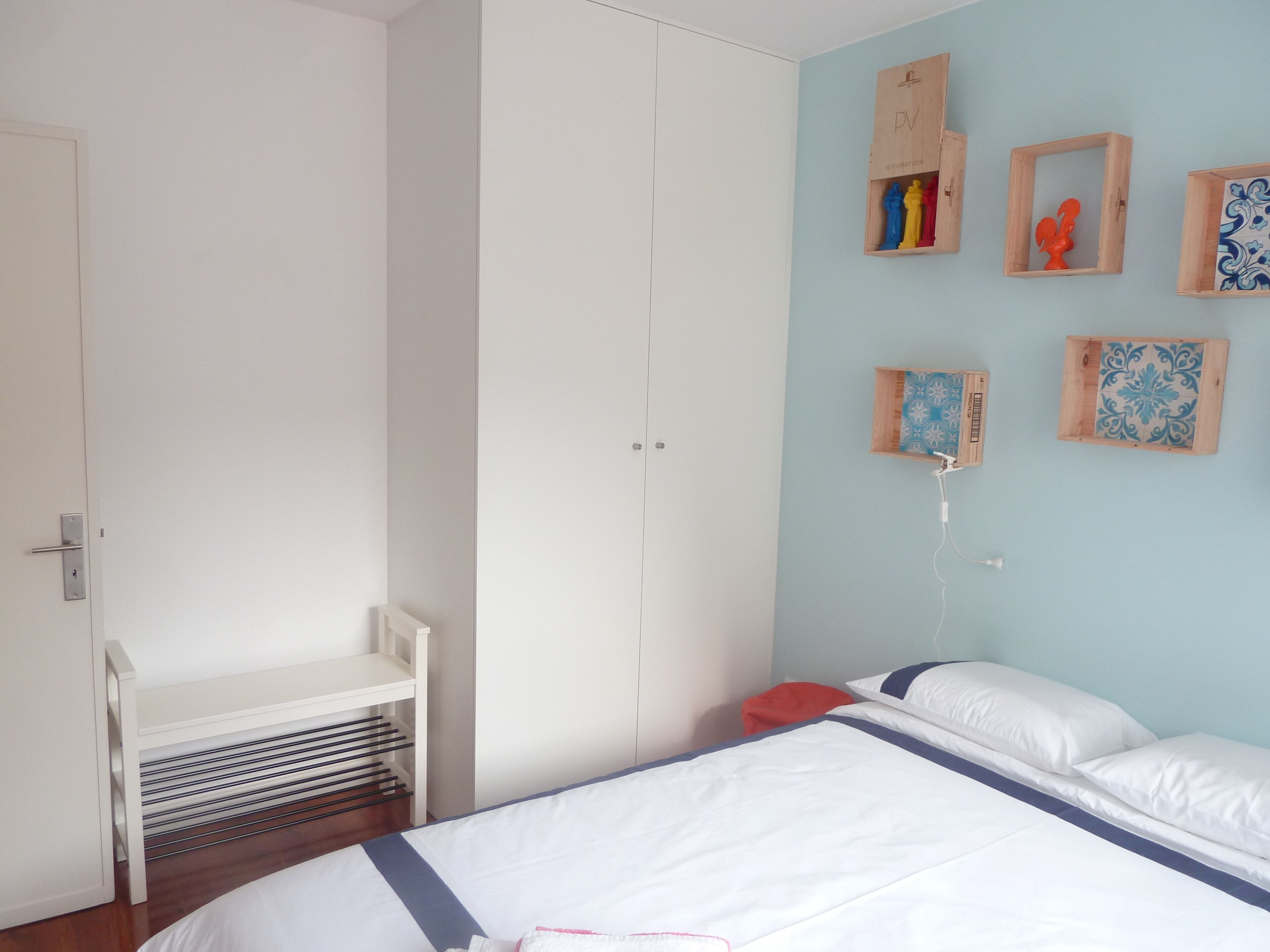 A bedroom with a bed, a white wardrobe, a small white bench, and decorative wall art.