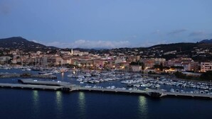 A marina with numerous boats docked, a town in the background with buildings and a hill, and a clear sky. - AIR-CONDITIONED T2 WITH SEA VIEW IN THE HEART OF PRORPRIANO, ON THE BEACH, 5 M FROM SHOPS (Propriano)