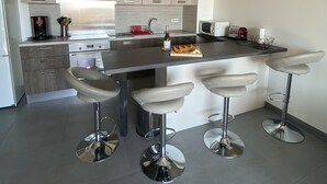 A modern kitchen with a central island, bar stools, stainless steel appliances, and light wood cabinetry. - AIR-CONDITIONED T2 WITH SEA VIEW IN THE HEART OF PRORPRIANO, ON THE BEACH, 5 M FROM SHOPS (Propriano)