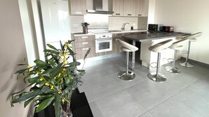A modern kitchen with a refrigerator, stove, and bar stools. - AIR-CONDITIONED T2 WITH SEA VIEW IN THE HEART OF PRORPRIANO, ON THE BEACH, 5 M FROM SHOPS (Propriano)