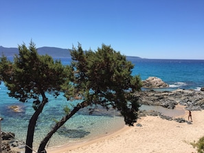 Une plage avec une eau claire, un rivage rocheux et une personne qui se promène.