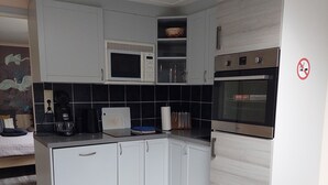 Une cuisine compacte avec des meubles blancs, un four à micro-ondes, un four encastré et une machine à café.