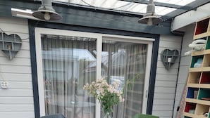 Une terrasse extérieure avec une table ronde et quatre chaises, un vase rempli de fleurs et une bibliothèque avec des boîtes de rangement colorées.
