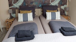 Une chambre double avec deux lits, chacun étant équipé d’une couette et d’oreillers. Un mur est décoré d’une fresque représentant des oiseaux et du feuillage.