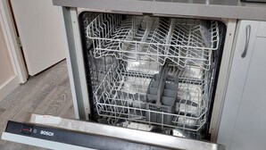 Un lave-vaisselle Bosch dans une cuisine avec un mur recouvert de carreaux et une machine à café posée sur le plan de travail.