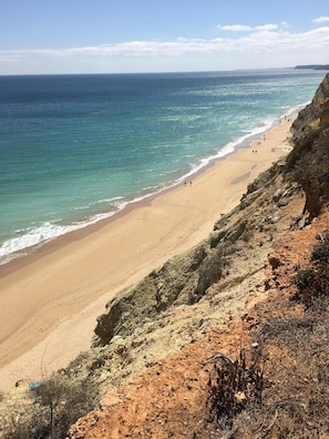Uma praia costeira com areal arenoso e falésias rochosas.