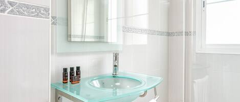 A bathroom with a glass sink, a mirror, and a shower.